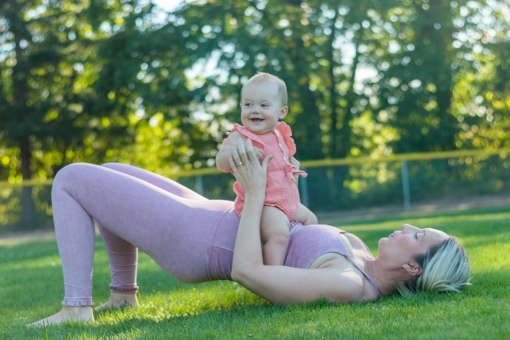 mom doing pelvic floor exercises on the lawn while holding her baby against her tummy