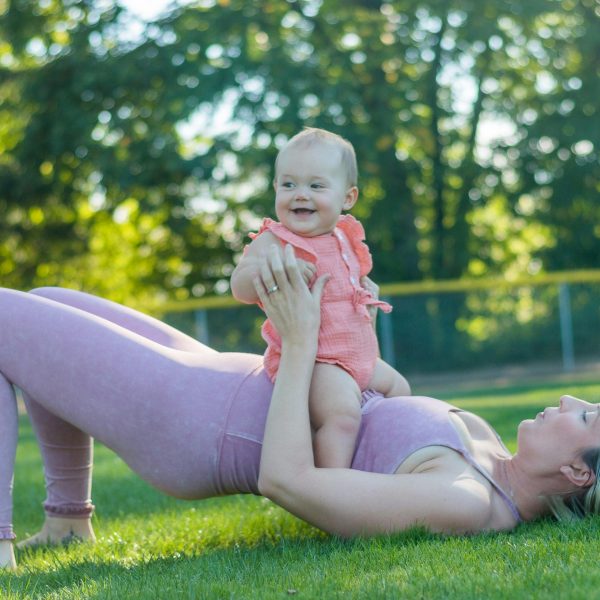 mom doing pelvic floor exercises on the lawn while holding her baby against her tummy